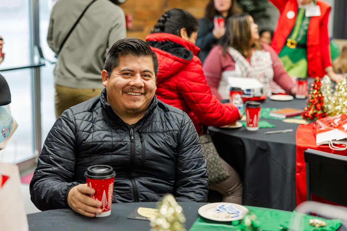 A dad smiles with a cup of coffee at the Christmas Store hospitality area